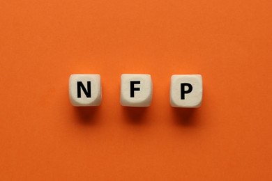 Photo of Abbreviation NFP (Nonfarm Payroll) made of cubes with letters on orange background, flat lay