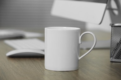 White ceramic mug on wooden table at workplace. Mockup for design