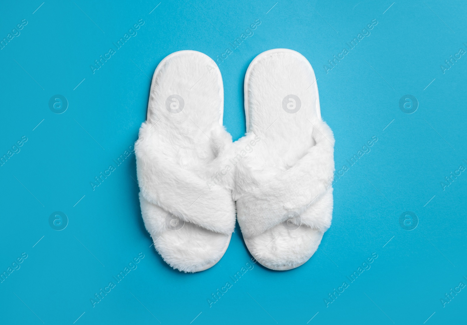 Photo of Pair of soft fluffy slippers on blue background, top view