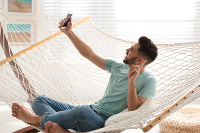Young man taking selfie in hammock at home