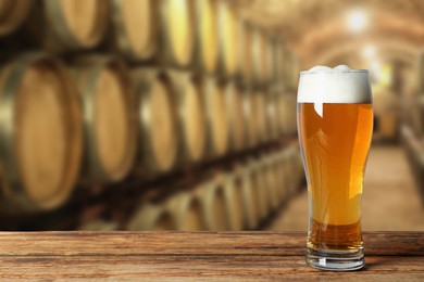 Image of Glass with fresh beer on wooden table in cellar, space for text