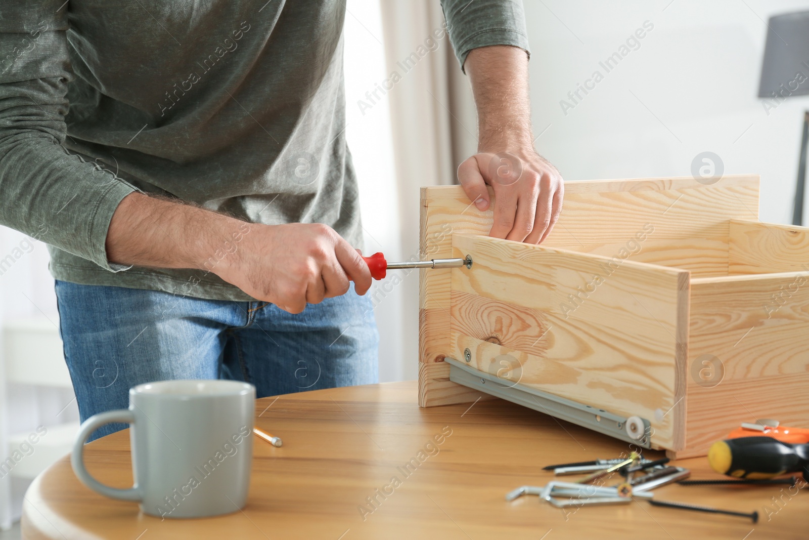 Photo of Young working man repairing drawer at home, closeup