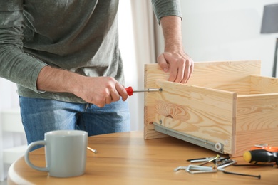 Young working man repairing drawer at home, closeup