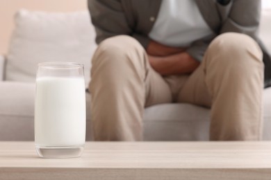 Photo of Man suffering from lactose intolerance at home, focus on glass of milk. Space for text