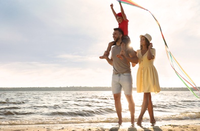 Happy parents and their child playing with kite on beach near sea. Spending time in nature