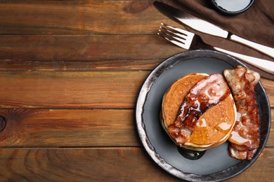 Photo of Delicious pancakes with maple syrup and fried bacon on wooden table, flat lay. Space for text