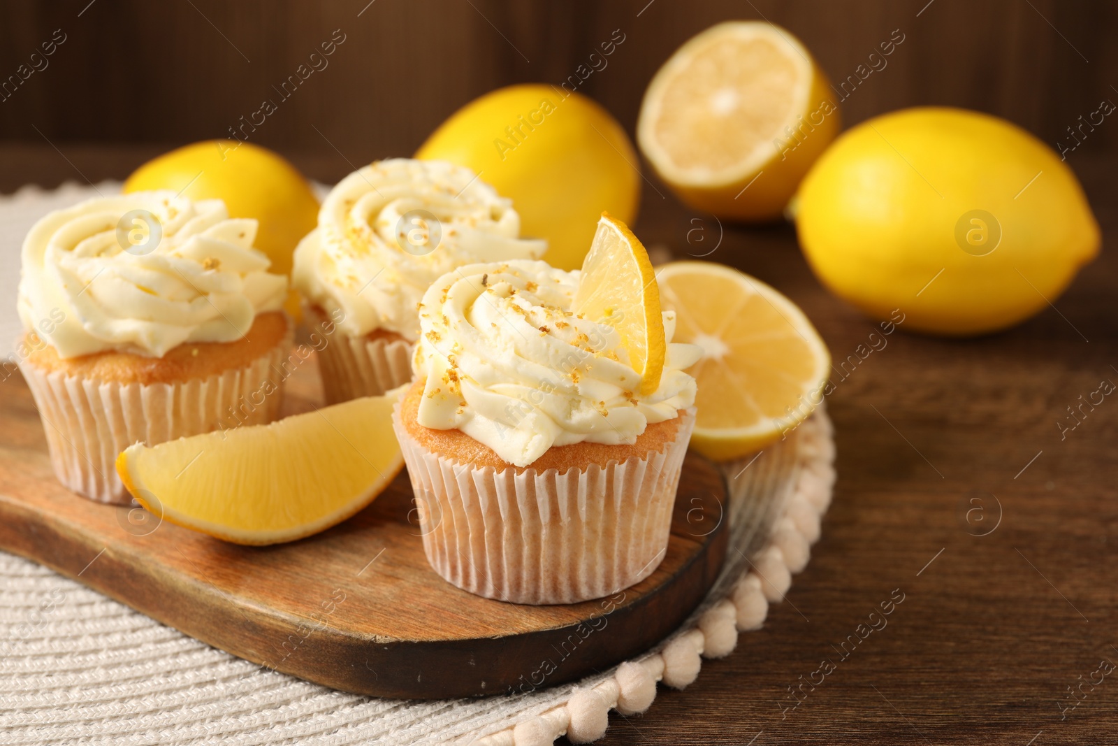 Photo of Tasty cupcakes with cream, zest and lemons on wooden table. Space for text