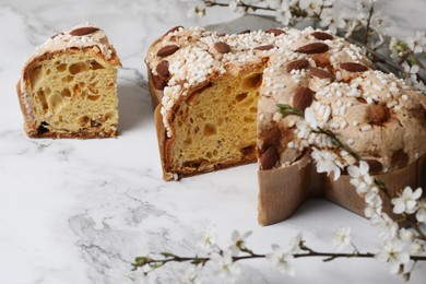 Photo of Delicious Italian Easter dove cake (traditional Colomba di Pasqua) and flowers on white marble table, closeup