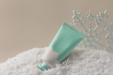 Photo of Winter skin care. Hand cream and decorative snowflake on artificial snow against light grey background, space for text