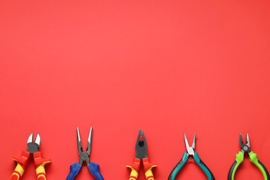 Photo of Different pliers on red background, flat lay. Space for text