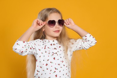 Photo of Girl wearing stylish sunglasses in shape of hearts on orange background