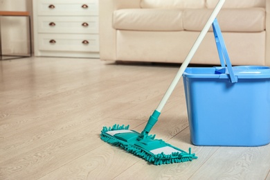 Mop and bucket on floor in living room, space for text. Cleaning service