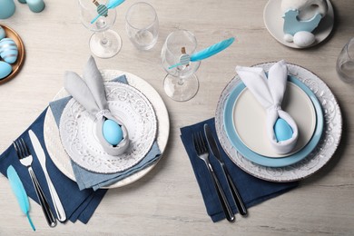 Photo of Festive table setting with bunny ears made of light blue eggs and napkins, above view. Easter celebration