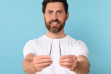 Photo of Happy man with tongue cleaner on light blue background, selective focus