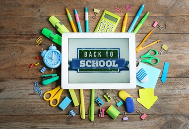 Tablet with phrase "BACK TO SCHOOL" and different stationery on wooden background, flat lay