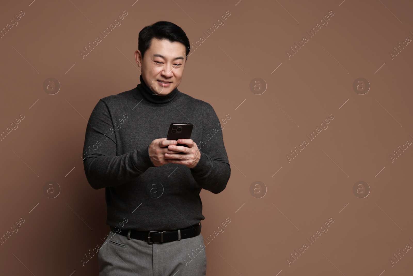 Photo of Portrait of happy man with smartphone on brown background. Space for text