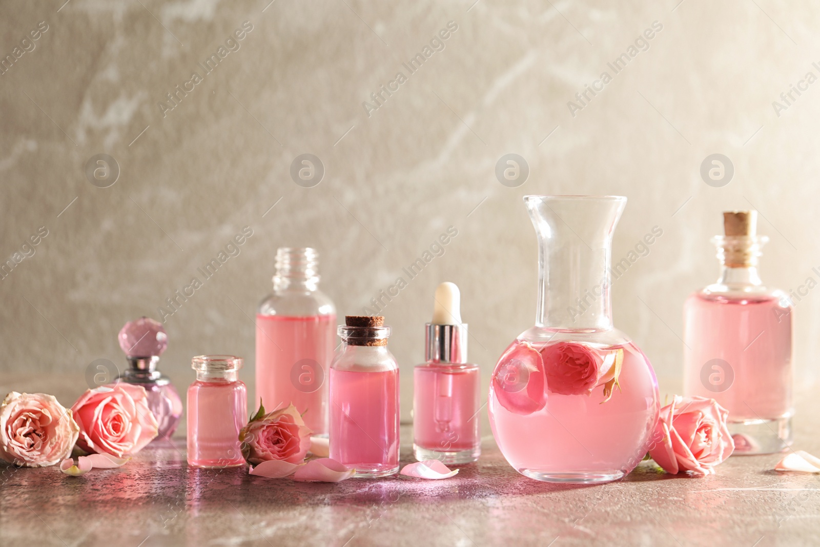 Photo of Composition with rose essential oil and flowers on table