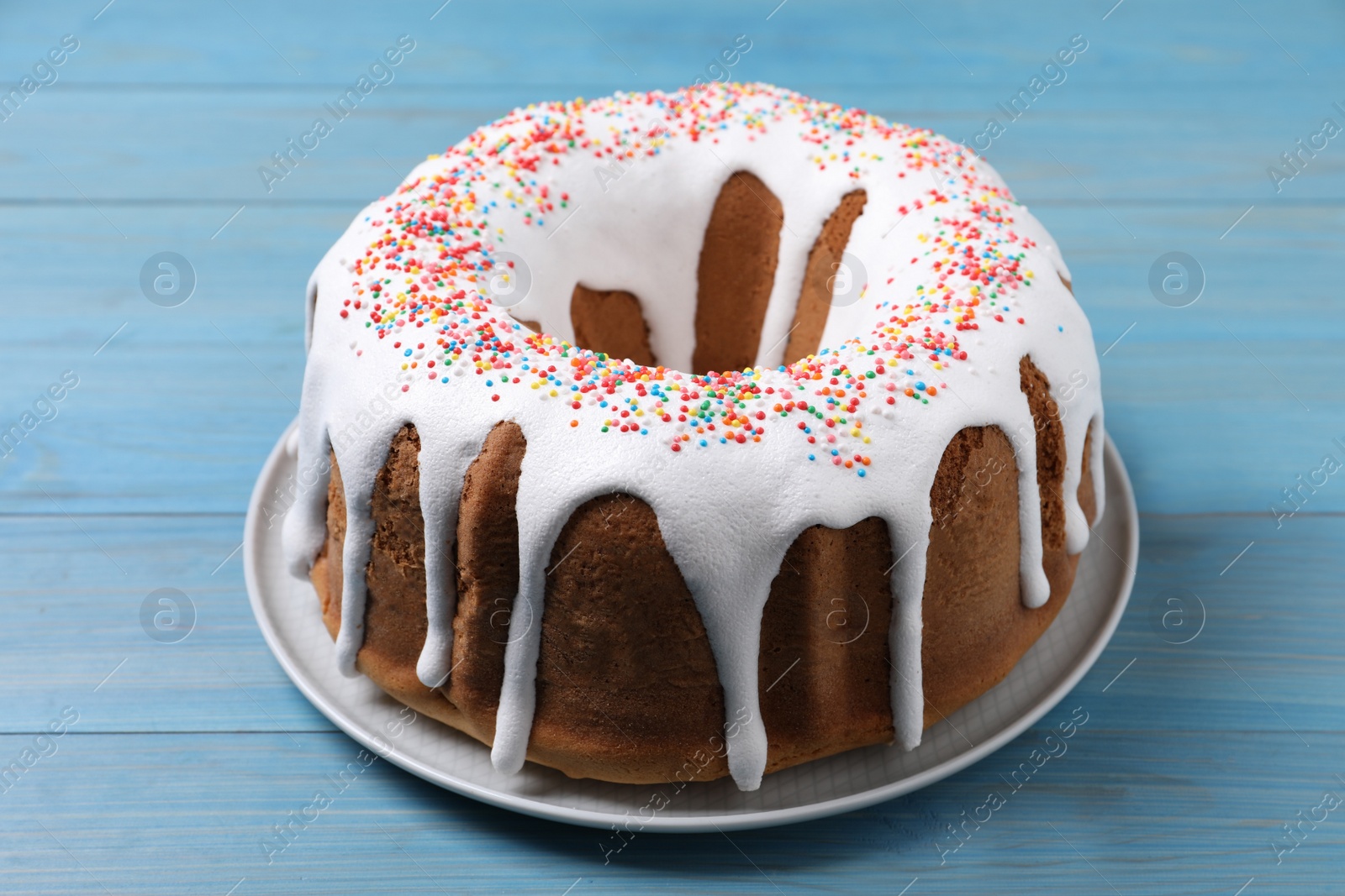 Photo of Glazed Easter cake with sprinkles on light blue wooden table