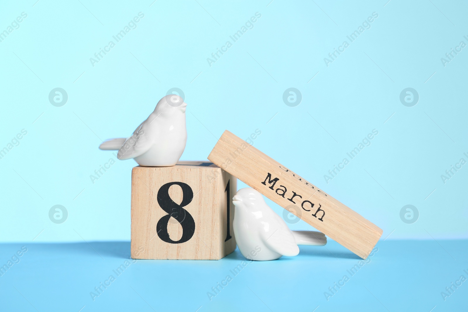 Photo of Wooden calendar and decorative birds on table against color background, space for text. International Women's Day