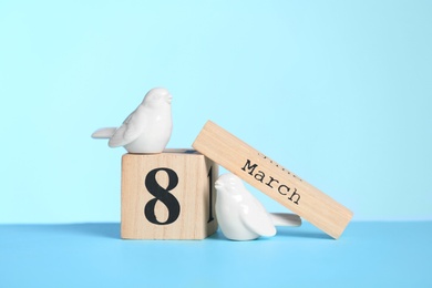 Photo of Wooden calendar and decorative birds on table against color background, space for text. International Women's Day