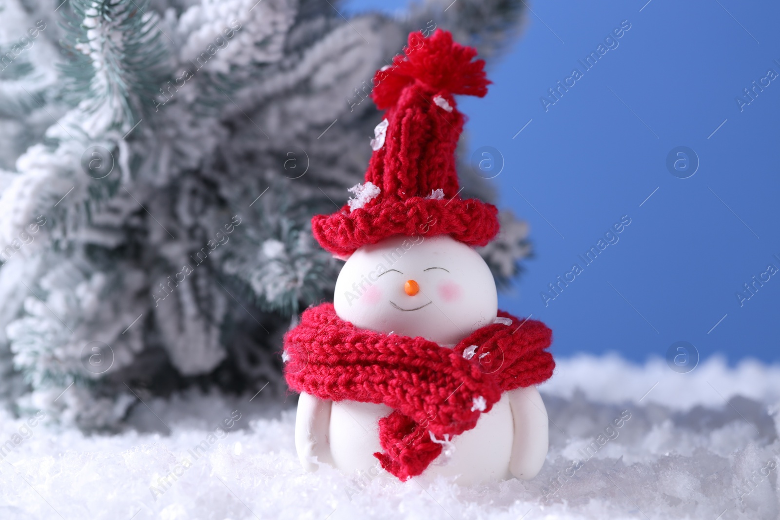 Photo of Cute decorative snowman and fir tree on artificial snow against light blue background, closeup