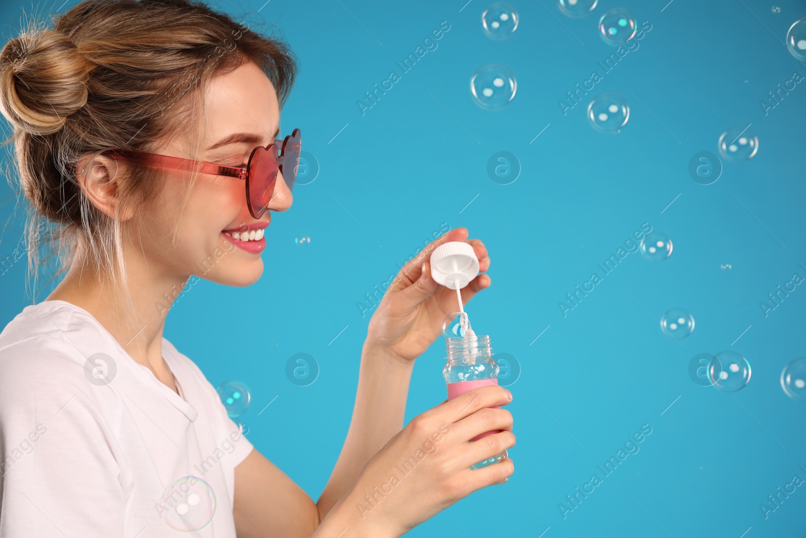 Photo of Young woman blowing soap bubbles on light blue background, space for text