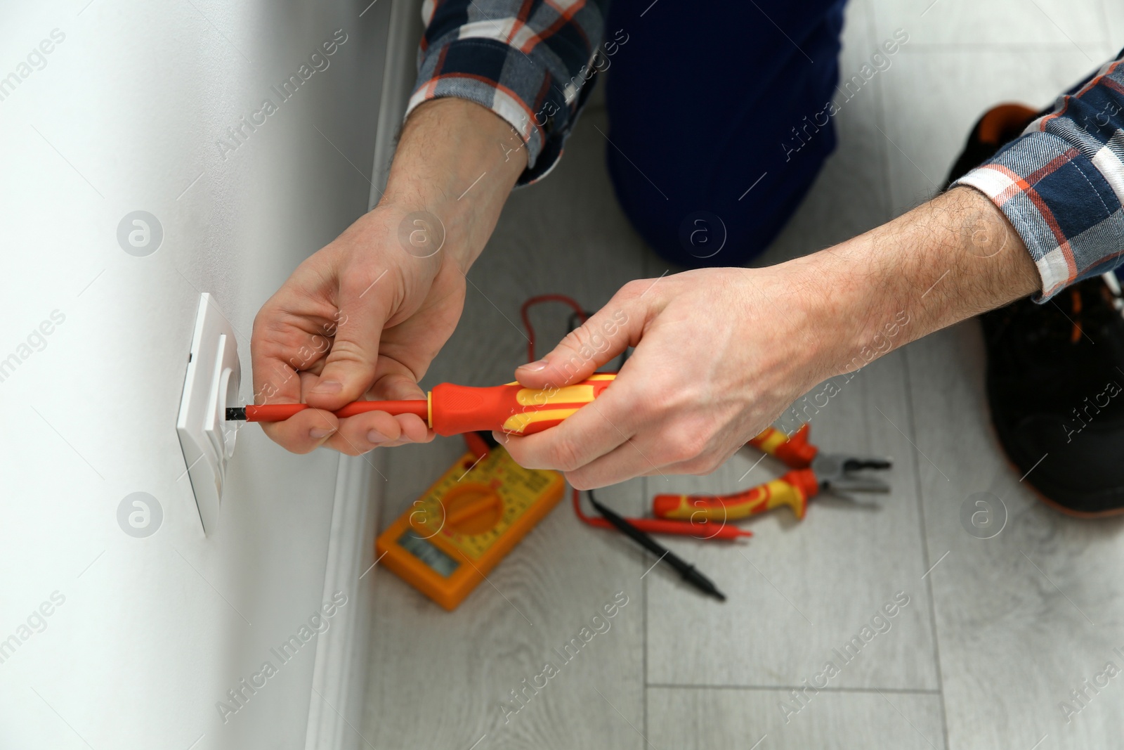 Photo of Electrician with screwdriver repairing power socket indoors, closeup