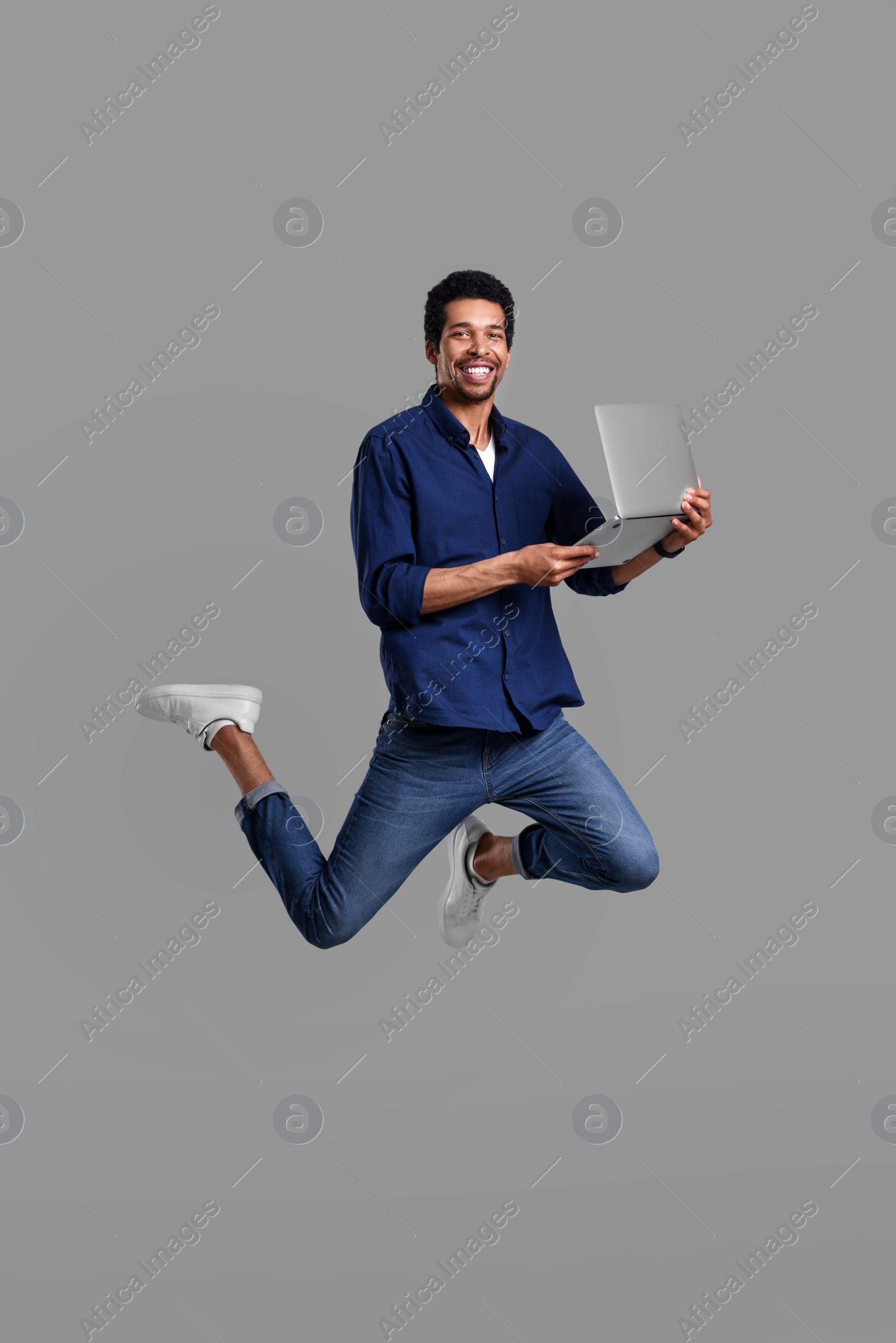 Photo of Happy man with laptop jumping on grey background