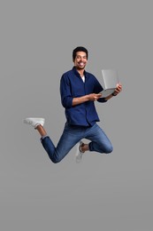 Happy man with laptop jumping on grey background