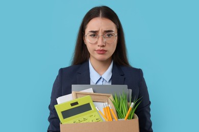 Photo of Unemployment problem. Unhappy woman with box of personal office belongings on light blue background