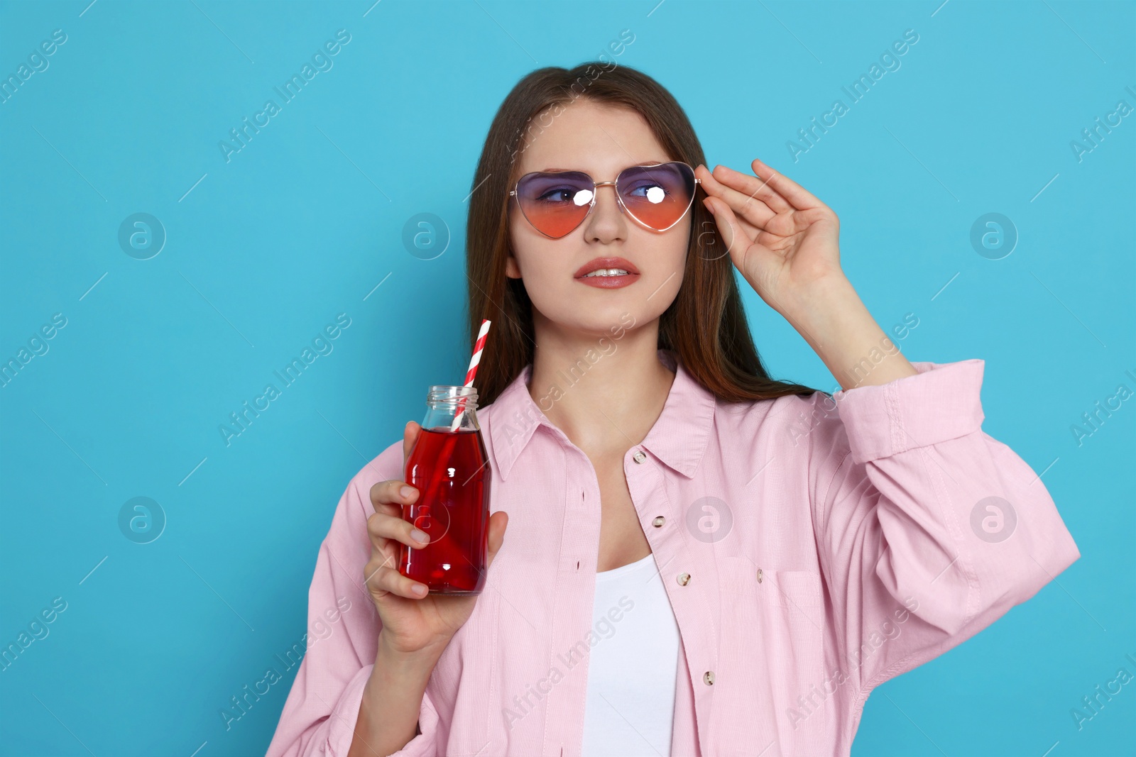 Photo of Beautiful young woman with glass bottle of juice on light blue background