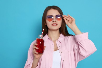 Beautiful young woman with glass bottle of juice on light blue background