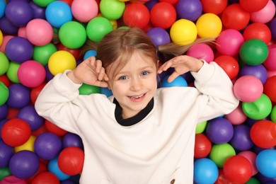 Happy little girl lying on many colorful balls, top view