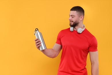 Photo of Handsome man with headphones and thermo bottle on yellow background, space for text