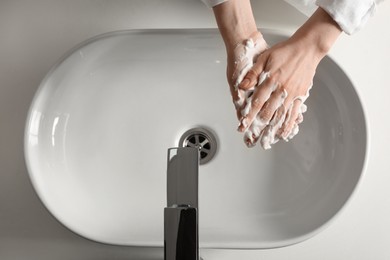 Woman washing hands with cleansing foam near sink in bathroom, top view