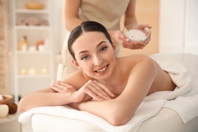 Beautiful young woman having massage with body scrub in spa salon