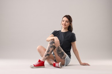 Photo of Smiling tattooed woman posing on grey background