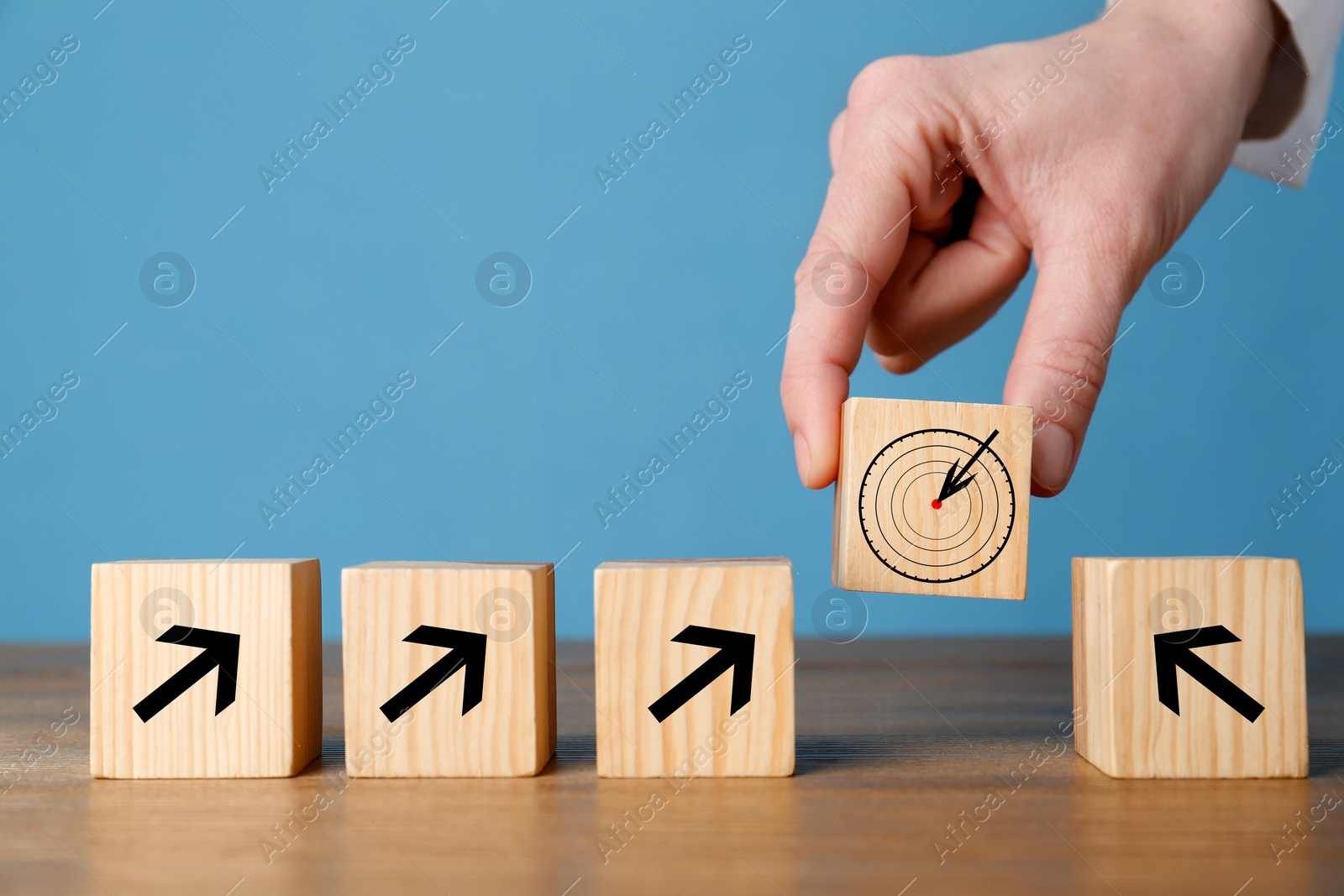 Image of Woman putting cube with icon of target into row of cubes with arrows against light blue background, closeup