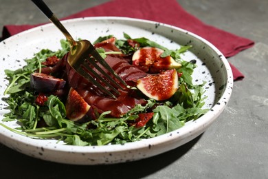 Photo of Eating tasty bresaola salad with fork on grey table, closeup
