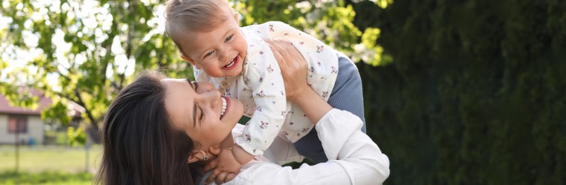 Image of Happy mother playing with her cute baby in park on sunny day. Banner design