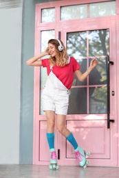 Photo of Happy girl with retro roller skates standing near pink door