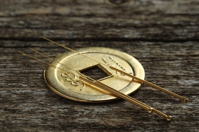 Photo of Acupuncture needles and Chinese coin on wooden table, closeup