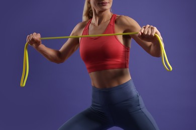 Photo of Woman exercising with elastic resistance band on purple background, closeup