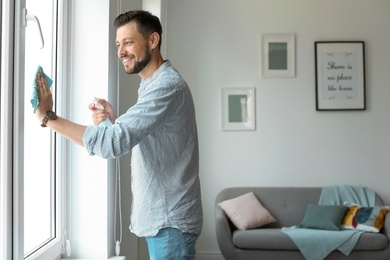 Man in casual clothes washing window glass at home