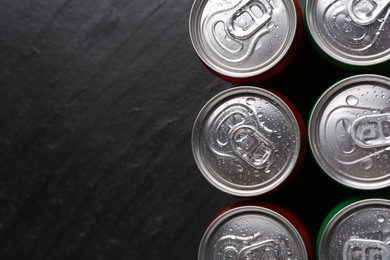 Photo of Energy drink in wet cans on black textured background, top view. Space for text