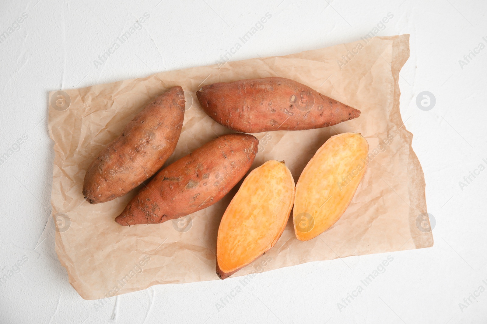 Photo of Parchment with cut and whole sweet potatoes on white table, top view