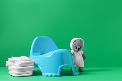 Photo of Light blue baby potty, diapers and toy on green background, space for text. Toilet training