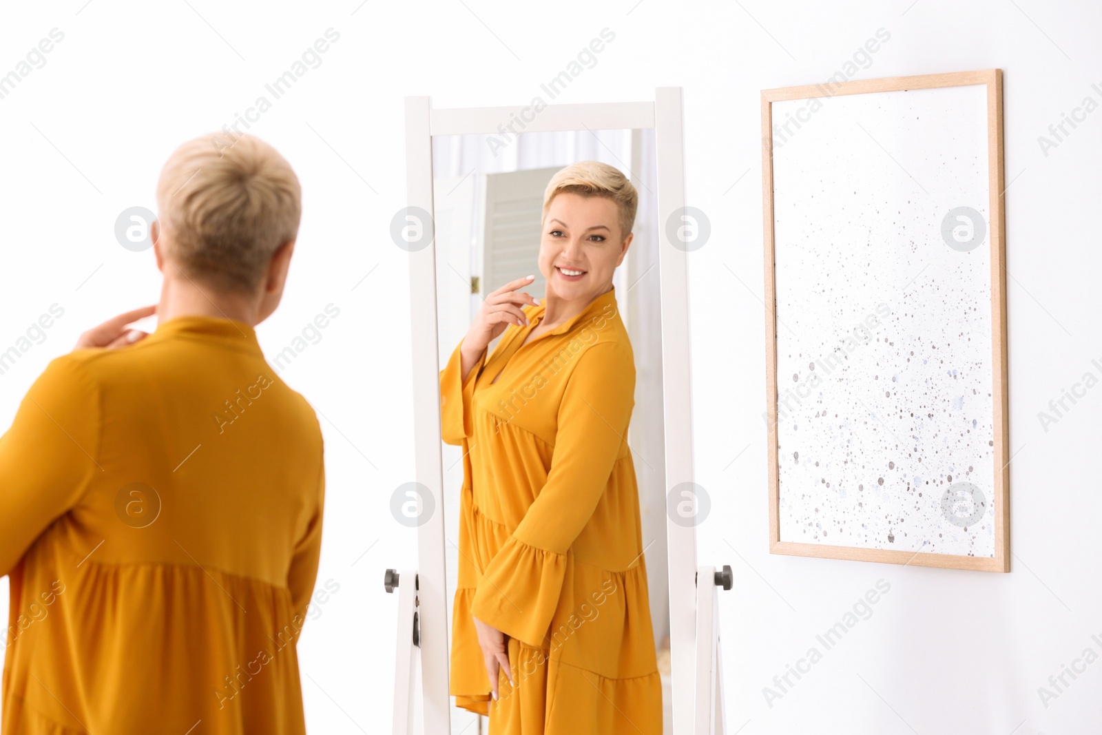 Photo of Beautiful mature woman looking at herself in large mirror indoors