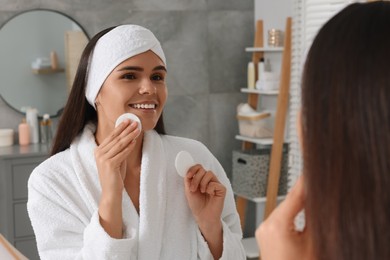 Photo of Young woman with cotton pads near mirror in bathroom