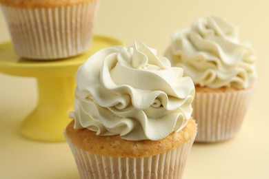 Tasty vanilla cupcakes with cream on pale yellow background, closeup